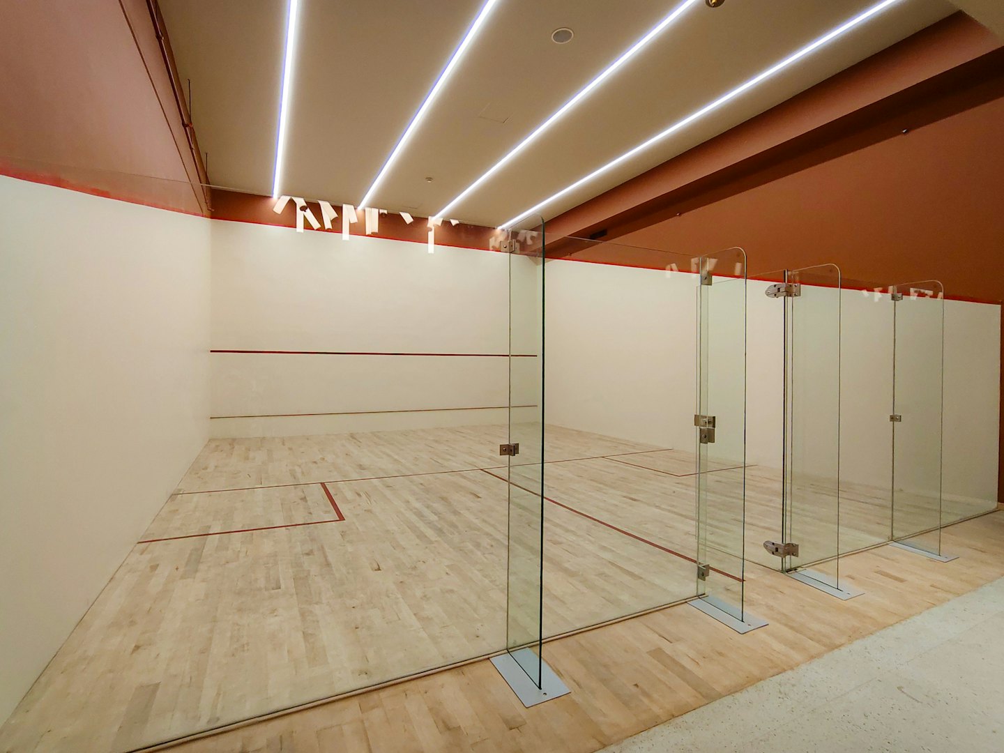 Moderni tyhjä squash-kenttä puisilla lattioilla ja lasiseinillä.